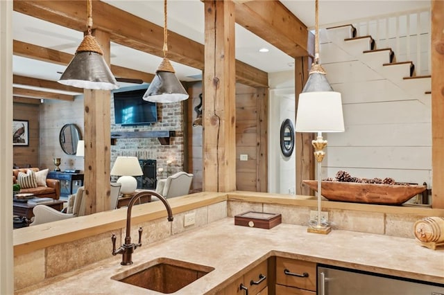 kitchen featuring a brick fireplace, wood walls, hanging light fixtures, and sink