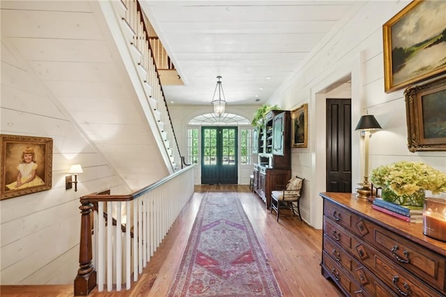 corridor featuring wood-type flooring, wooden walls, and french doors