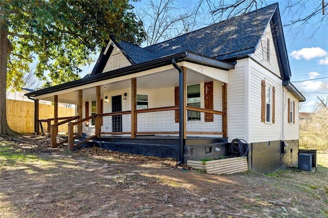 view of front of home with covered porch, central AC, roof with shingles, and fence