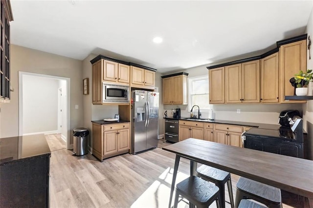 kitchen featuring dark countertops, light wood-style flooring, light brown cabinetry, appliances with stainless steel finishes, and a sink