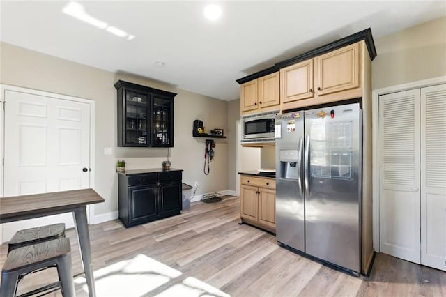 kitchen featuring light wood finished floors, stainless steel appliances, glass insert cabinets, light brown cabinets, and baseboards