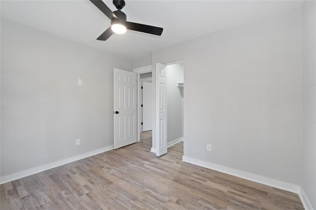 unfurnished bedroom with a spacious closet, baseboards, ceiling fan, and wood finished floors