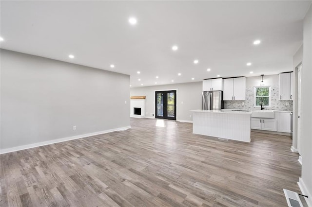 unfurnished living room with a sink, baseboards, light wood finished floors, and recessed lighting