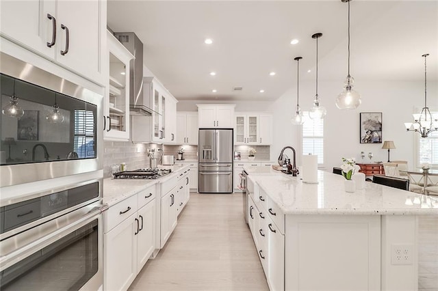 kitchen featuring decorative light fixtures, tasteful backsplash, an island with sink, white cabinets, and stainless steel appliances