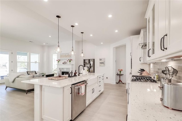 kitchen with white cabinets, hanging light fixtures, stainless steel appliances, light stone countertops, and a center island with sink