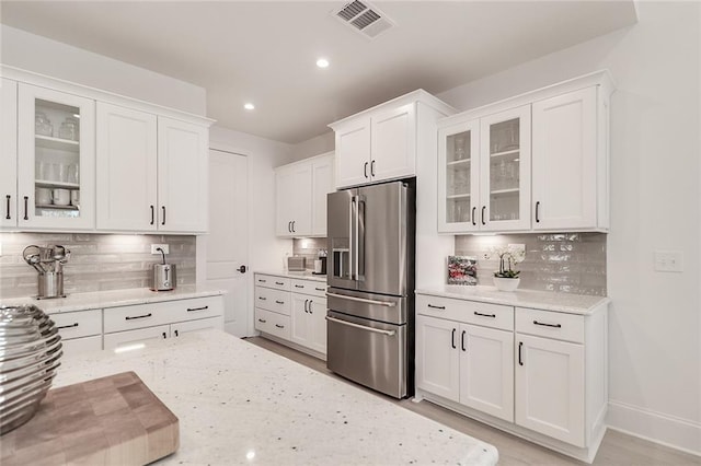 kitchen featuring light stone counters, high end refrigerator, backsplash, and white cabinets