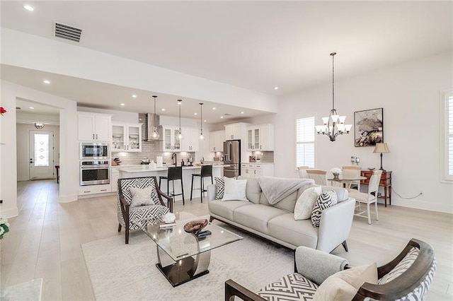 living room featuring sink, light hardwood / wood-style flooring, and a notable chandelier