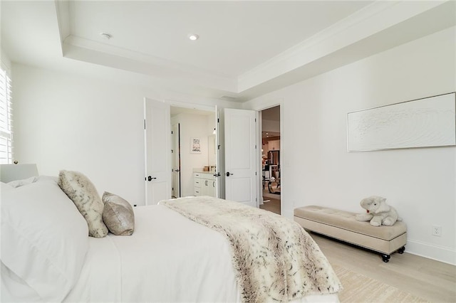 bedroom with connected bathroom, light hardwood / wood-style floors, and a raised ceiling