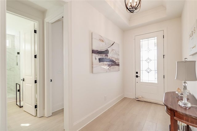 entryway featuring an inviting chandelier, a wealth of natural light, light wood-type flooring, and a tray ceiling