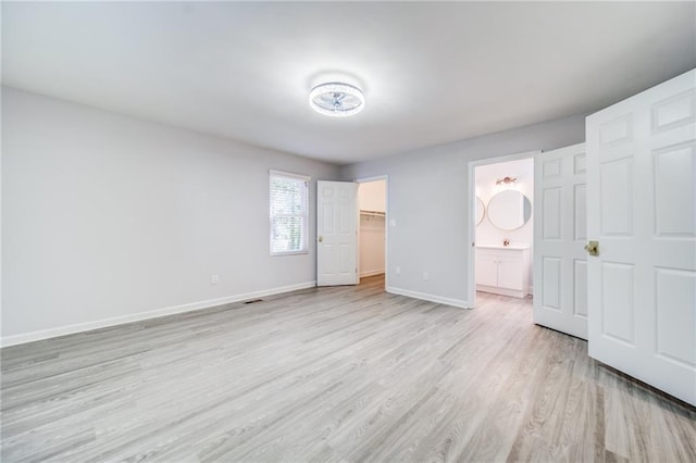 unfurnished bedroom with a walk in closet, connected bathroom, a closet, and light wood-type flooring