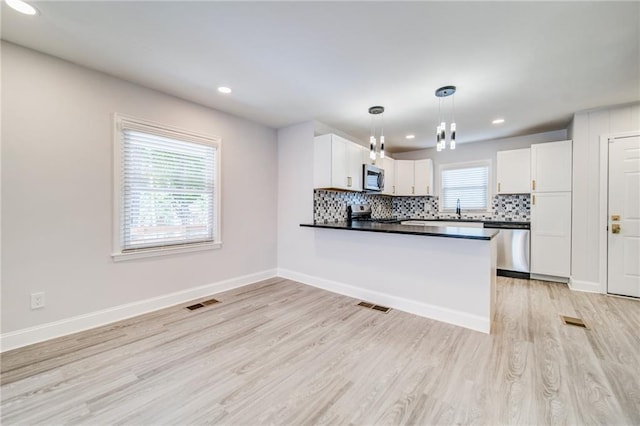 kitchen with tasteful backsplash, appliances with stainless steel finishes, white cabinets, and decorative light fixtures