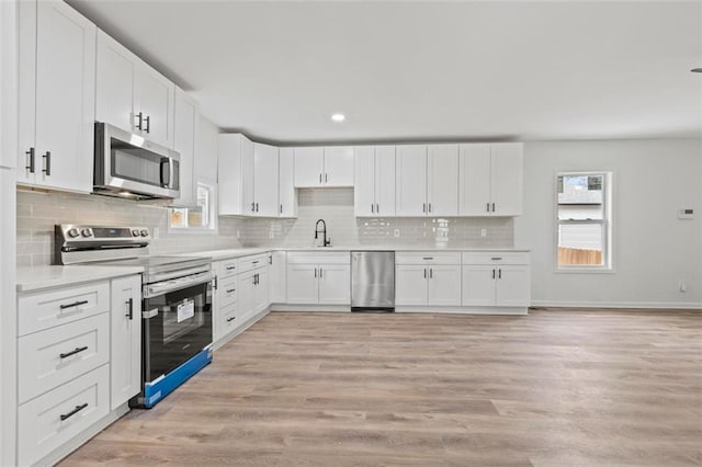 kitchen featuring sink, light hardwood / wood-style flooring, white cabinetry, stainless steel appliances, and tasteful backsplash