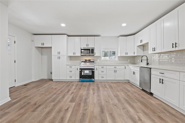 kitchen featuring sink, appliances with stainless steel finishes, tasteful backsplash, light hardwood / wood-style floors, and white cabinets