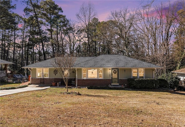 ranch-style house featuring a shingled roof, a front yard, and brick siding