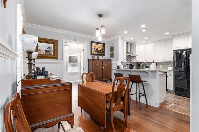 dining space with wainscoting, recessed lighting, wood finished floors, and crown molding