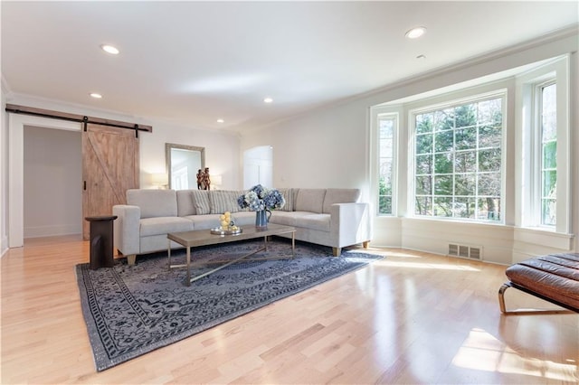 living area with a barn door, visible vents, light wood-style flooring, and recessed lighting