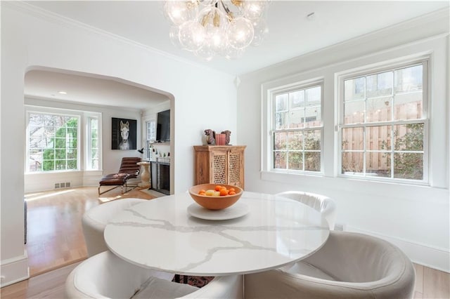 dining room featuring ornamental molding, arched walkways, visible vents, and wood finished floors