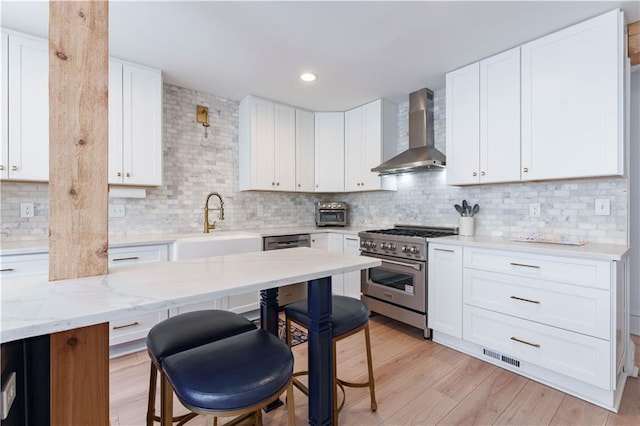 kitchen featuring stainless steel stove, a sink, light wood-type flooring, decorative backsplash, and wall chimney exhaust hood