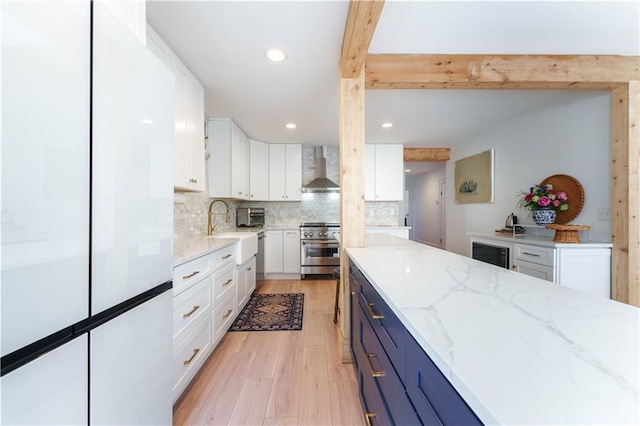 kitchen featuring white cabinets, wall chimney exhaust hood, beamed ceiling, high end stainless steel range oven, and a sink