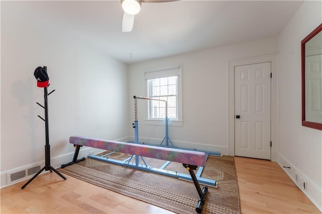 workout room featuring a ceiling fan, visible vents, baseboards, and wood finished floors