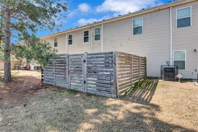 back of property with a yard, central AC unit, and fence