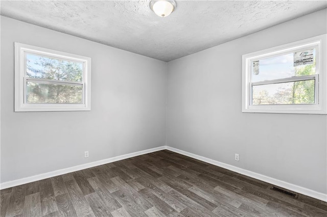 spare room featuring a textured ceiling, dark hardwood / wood-style flooring, and a wealth of natural light