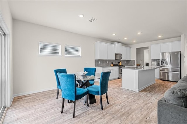 kitchen with white cabinets, appliances with stainless steel finishes, sink, a kitchen island with sink, and light hardwood / wood-style flooring