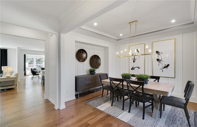 dining space with a raised ceiling, a notable chandelier, ornamental molding, and wood finished floors