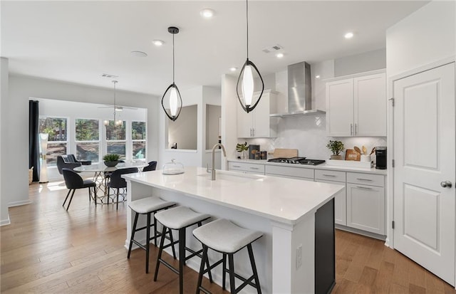 kitchen with a sink, visible vents, a breakfast bar, wall chimney exhaust hood, and stainless steel gas cooktop