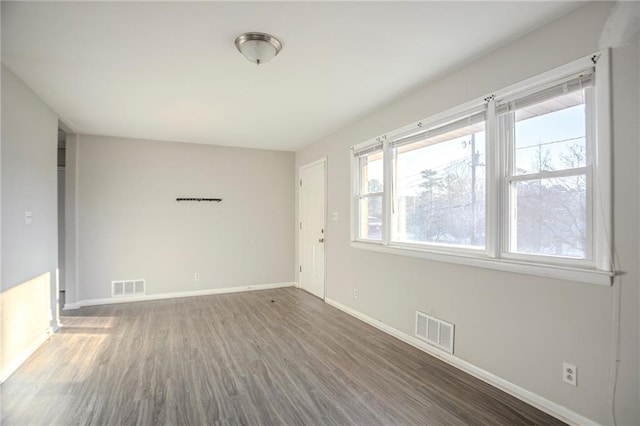 empty room with wood finished floors, visible vents, and baseboards