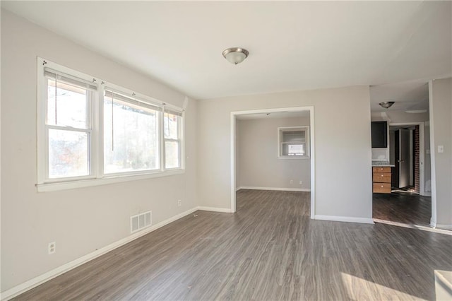 empty room with dark wood-style flooring, visible vents, and baseboards