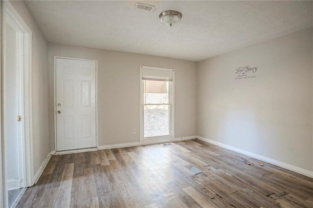 empty room featuring wood finished floors, visible vents, and baseboards