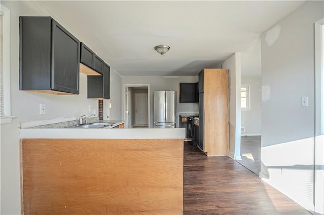 kitchen featuring freestanding refrigerator, light countertops, a sink, and a peninsula