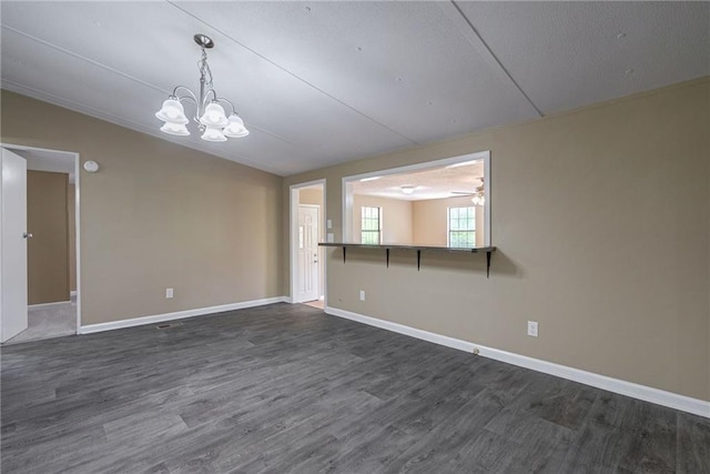 empty room with ceiling fan with notable chandelier, dark hardwood / wood-style floors, and lofted ceiling