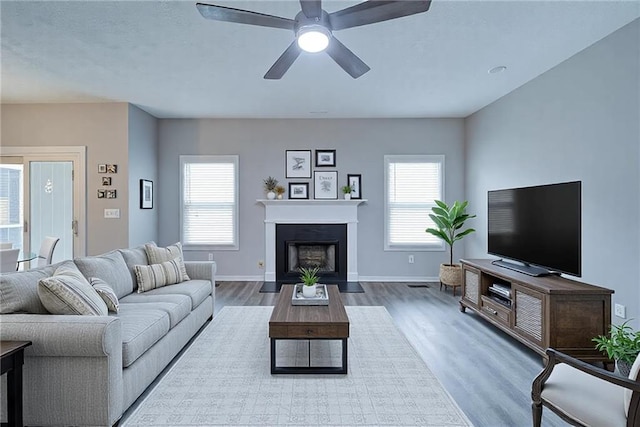 living room with a fireplace with flush hearth, baseboards, wood finished floors, and ceiling fan