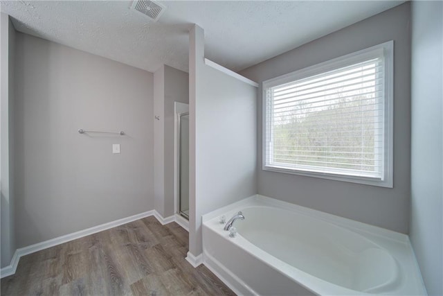 full bath with a textured ceiling, a stall shower, visible vents, wood finished floors, and a garden tub