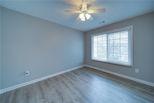 spare room featuring wood finished floors, visible vents, a ceiling fan, and baseboards