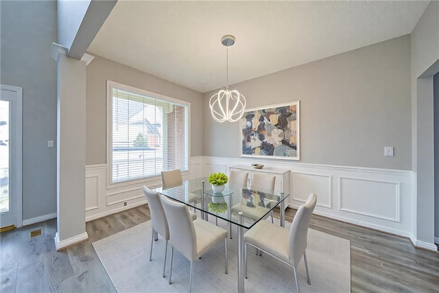 dining area featuring wood finished floors, a decorative wall, a wainscoted wall, and a notable chandelier