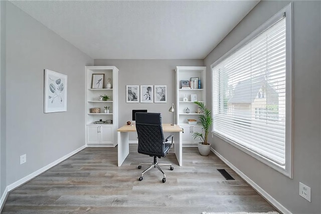 office space featuring wood finished floors, visible vents, built in features, and baseboards