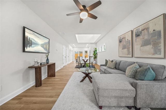 living room with a skylight, visible vents, ceiling fan, light wood-type flooring, and baseboards