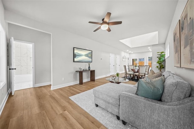 living room with light wood-style floors, a skylight, baseboards, and a ceiling fan