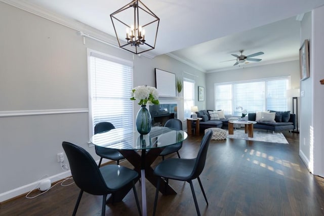 dining room with a tile fireplace, ceiling fan with notable chandelier, ornamental molding, and dark wood-type flooring