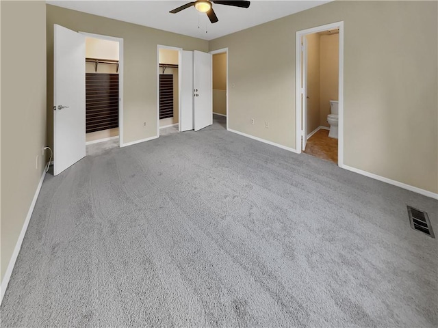 unfurnished bedroom featuring a walk in closet, carpet flooring, connected bathroom, and ceiling fan