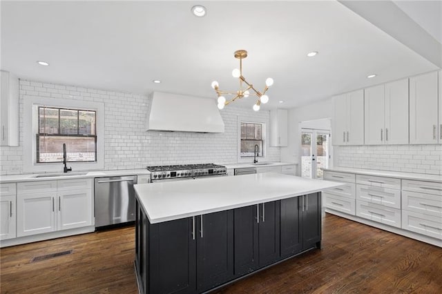 kitchen with dark cabinetry, a sink, stove, stainless steel dishwasher, and wall chimney exhaust hood