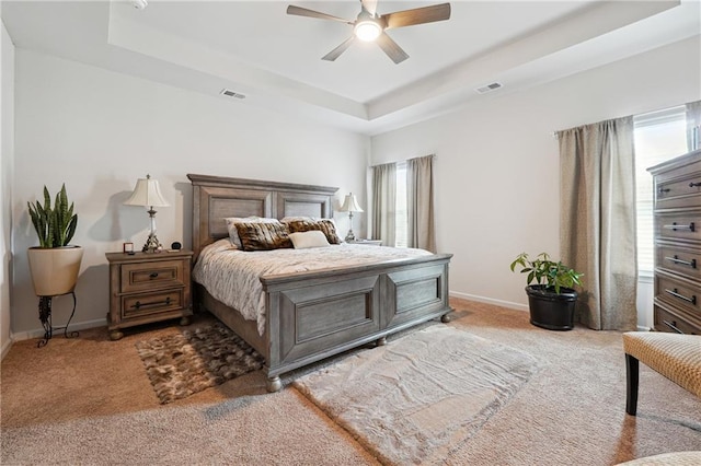 carpeted bedroom with ceiling fan and a tray ceiling