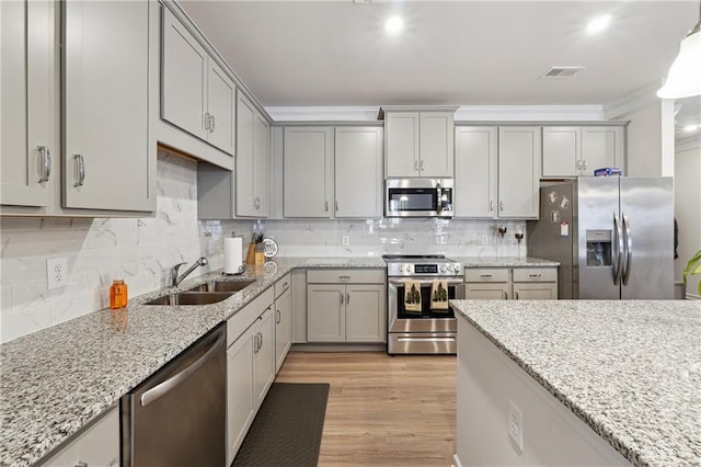 kitchen with light stone counters, ornamental molding, appliances with stainless steel finishes, and sink