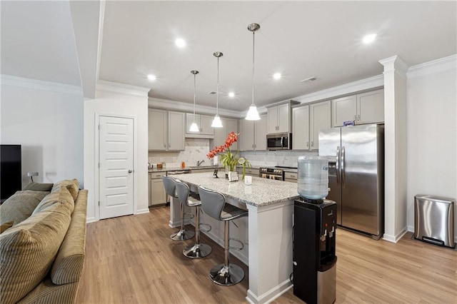 kitchen featuring appliances with stainless steel finishes, hanging light fixtures, light stone countertops, an island with sink, and a kitchen bar