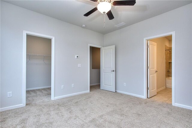 unfurnished bedroom with a walk in closet, ensuite bath, light colored carpet, ceiling fan, and a closet