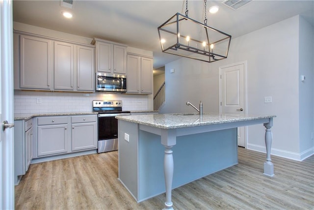 kitchen featuring hanging light fixtures, stainless steel appliances, light hardwood / wood-style flooring, a breakfast bar, and a center island with sink