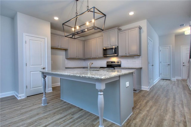 kitchen featuring a kitchen island with sink, hanging light fixtures, gray cabinets, appliances with stainless steel finishes, and light hardwood / wood-style floors